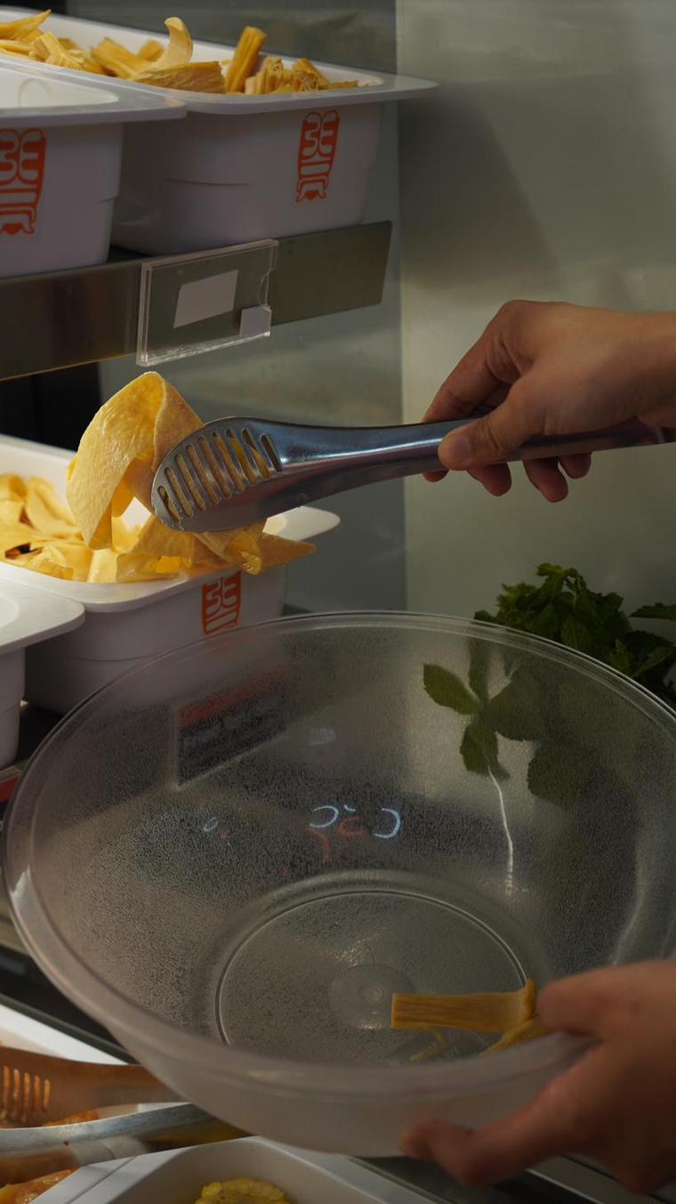 Une main dépose des feuilles de tofu dans un bol à l'aide d'une pince.
